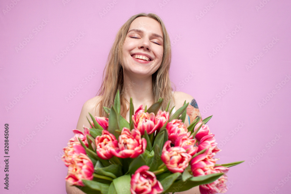 young beautiful girl with a bouquet of flowers on a colored pink background, a woman holds tulips and smiles