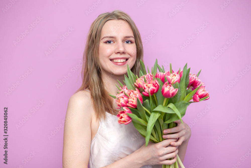 young beautiful girl with a bouquet of flowers on a colored pink background, a woman holds tulips and smiles