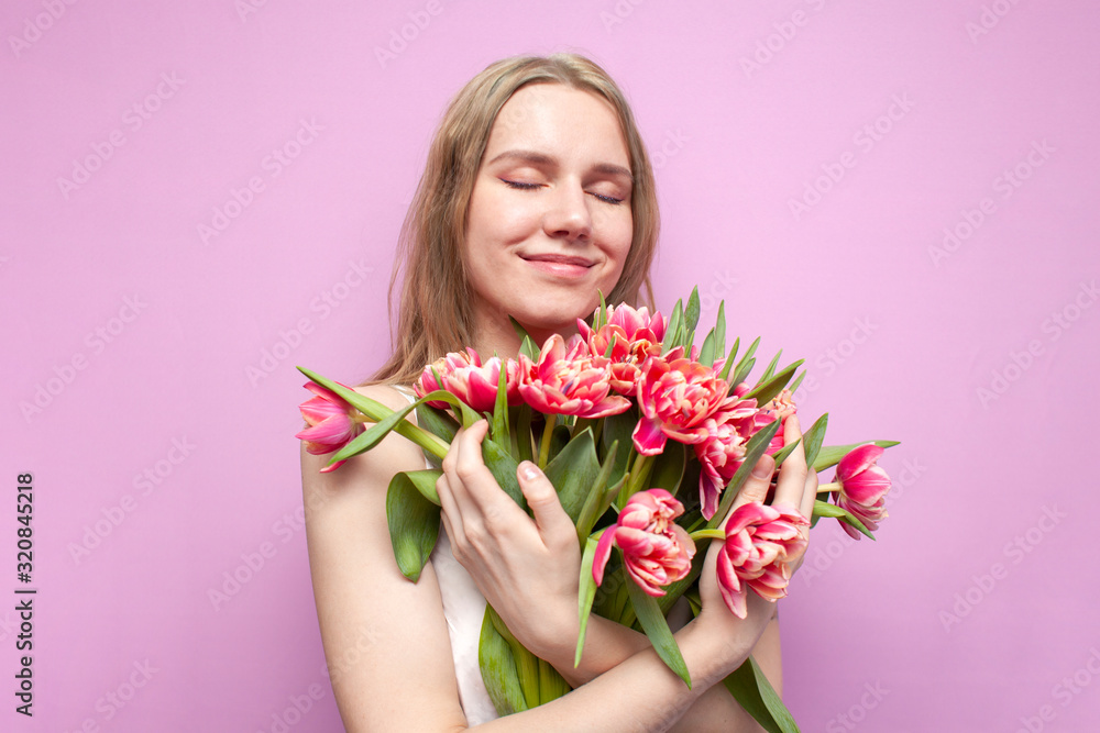 girl holds and sniffs a bouquet of flowers on a pink background, a beautiful woman with tulips