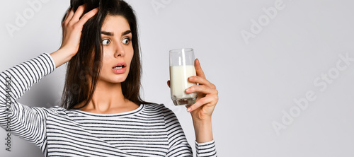 Excited young woman holding a glass of milk, not knowing whether to drink it or not milk.