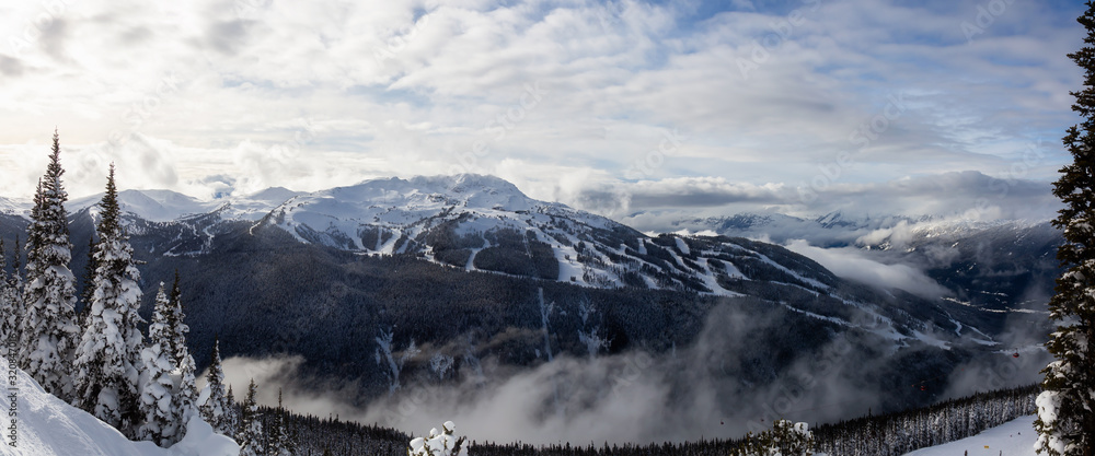 Fototapeta premium Whistler, British Columbia, Canada. Beautiful Panoramic View of the Canadian Snow Covered Mountain Landscape during a cloudy and vibrant winter day.