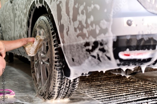  Hand a worker washing the top of a wheel disc, a fragment of the rear bumper of a car in soapy foam.