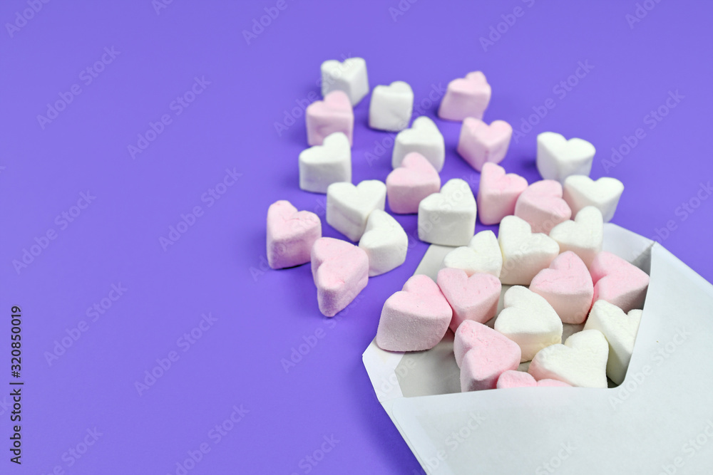 Pink and white heart shaped marshmallow hearts spilling out of white love letter envelope on purple background