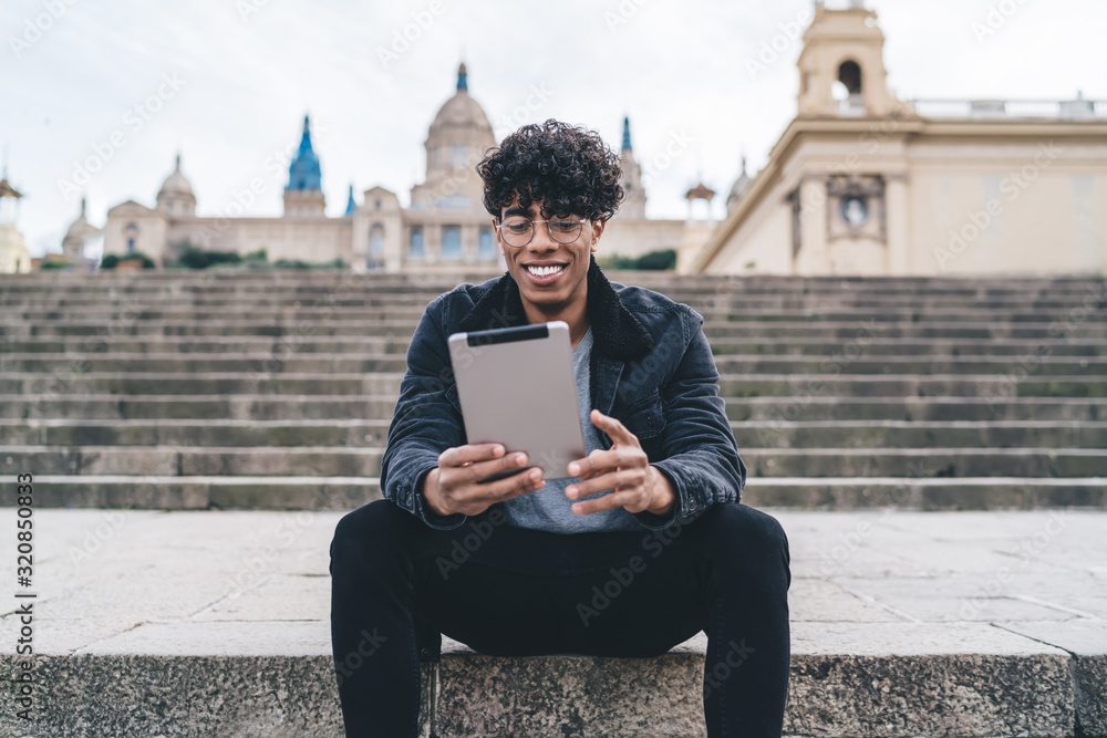 Obraz premium Cheerful African American man sitting on stairs and using tablet