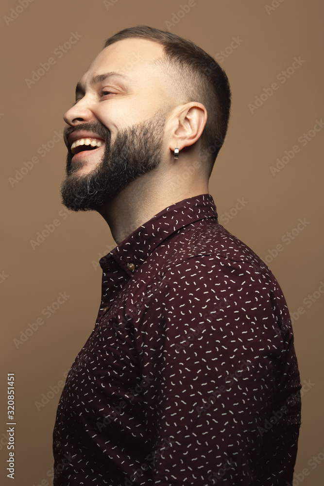 Fabulous at any age concept. Profile portrait of laughing 40-year-old man standing over beige background. Modern haircut. Hipster style. Close up. Studio shot Fabulous at any age concept. Profile portrait of laughing 40-year-old man standing over beige background. Modern haircut. Hipster style. Close up. Studio shot