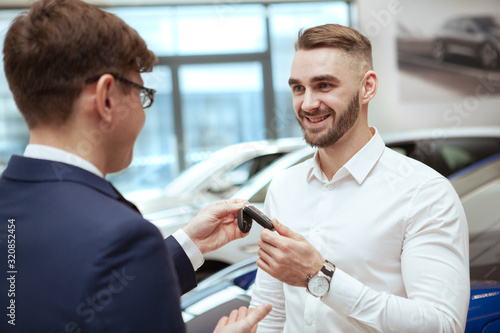 Happy handsome man smiling, receiving car keys from the sdalesdman at car dealership