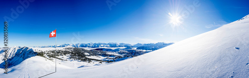 snow covered swiss alps mountain range with swiss national flag against blue sky, with copy space © Simon