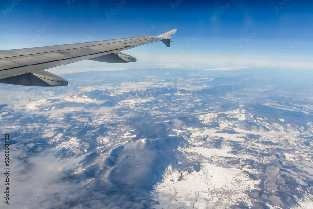 Obraz premium Plane silver wing during a flight over white clouds and a winter land is on the photo