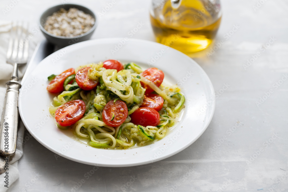 Spiral zucchini noodles with tomato on white plate on ceramic background