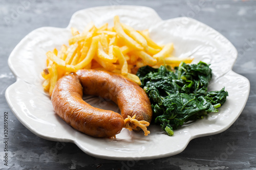 fried smoked sausage with potato chips and greens on beautiful plate on ceramic background photo