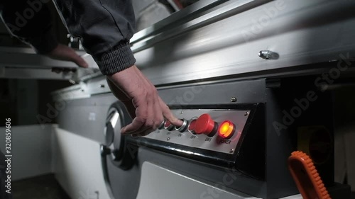 professional worker in overalls furniture factory includes electric machine for cutting wood. man presses buttons with fingers. construction and manufacturing sectors. enabling and disabling hardware