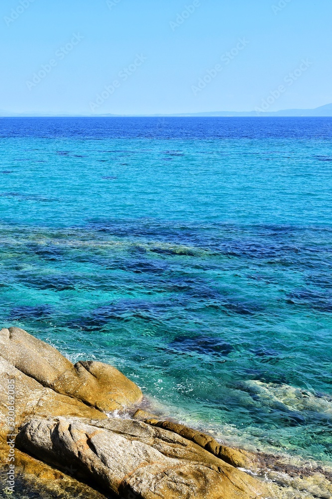 Amazing azure sea water and rocks. Beautiful natural beach with white stones and turquoise water. Halkidiki Greece Blue Flag Beach. Coral reef in the sea. White rocks and transparent ocean. Vertical 