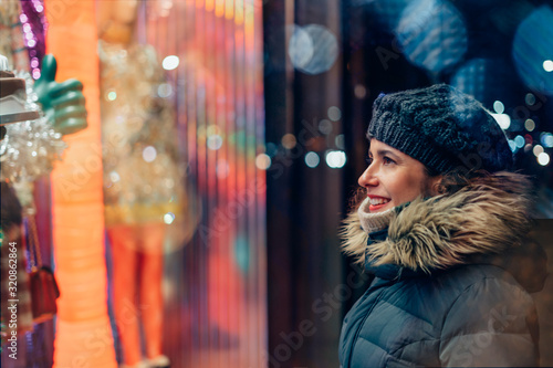 Beautiful girl with warm clothes looking at he showcase window on the night city street. Bokeh lights and copy space available