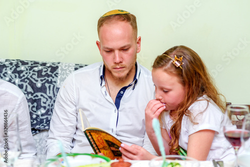 Family around the table for the traditional Passover dinner reading the Haggadah. Jewish family at the feast of Passover. Selective focus on man. photo