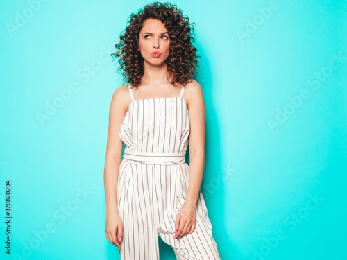 Portrait of beautiful smiling model with afro curls hairstyle dressed in summer hipster clothes.Sexy carefree girl posing in studio near blue wall.Trendy funny and positive woman