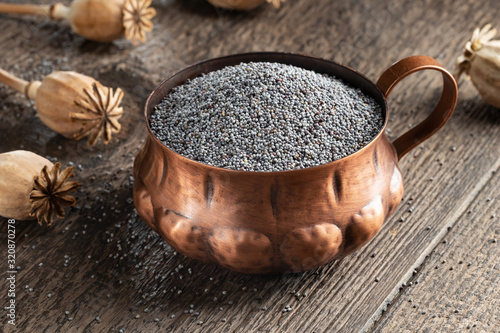 Poppy seeds in a vintage cup, with poppyheads in the background photo