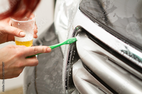 An employee of the car wash thoroughly washes conducts detaling and applies protective equipment to the body of an expensive car.