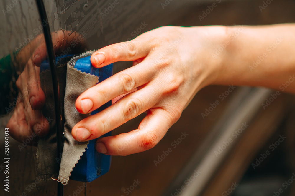 An employee of the car wash thoroughly washes conducts detaling and applies protective equipment to the body of an expensive car.