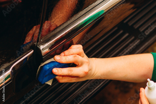 An employee of the car wash thoroughly washes conducts detaling and applies protective equipment to the body of an expensive car.