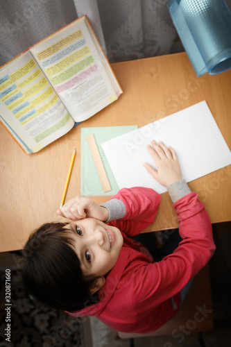 Smiling little asian schoolgirl doing homework.