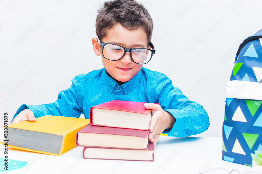 A little boy with glasses collects books. A smart little boy did all his homework. A successful little schoolboy is happy to get ready for school.