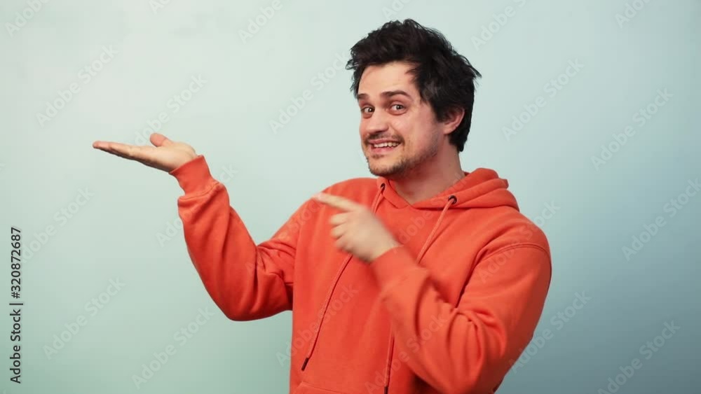 Guy in orange hoodie demonstrate something on blue background Guy in orange hoodie demonstrate something on blue background