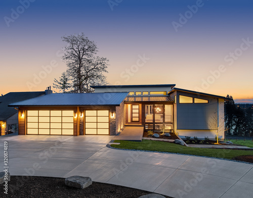 Beautiful modern style luxury home exterior at sunset with glowing interior lights. Features three car garage with translucent panels, clerestory windows and elegant design.