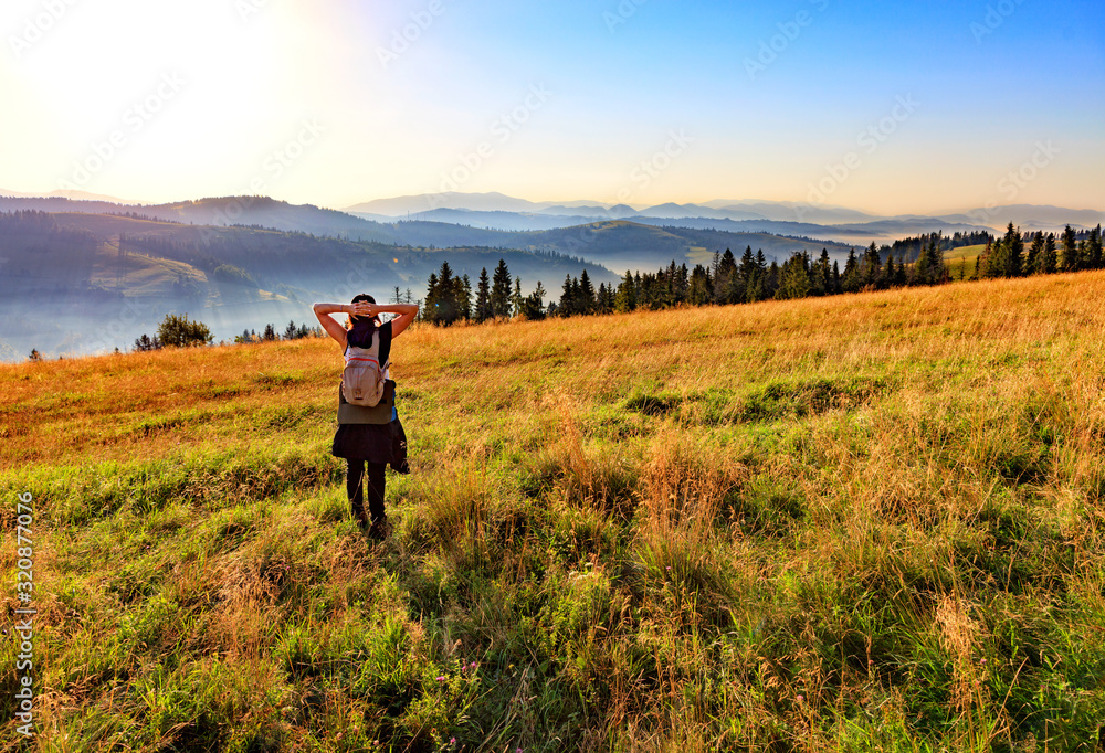 Young woman inhales the aroma of wild herbs and flowers at sunrise on a hilltop in the Carpathians.