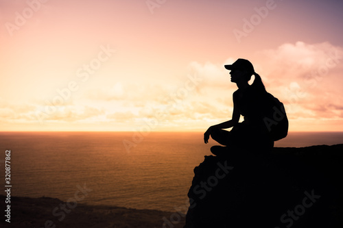 Looking to the future, new day, new beginning. Young female sitting on a mountain facing sunset