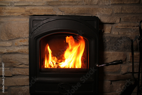 beautiful red flame of fire from burning firewood in an iron black fireplace, the concept of a cozy house