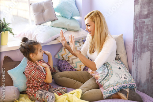 Tableau sur toile Happy smiled mother and daughter are clapping together hands in bright room near