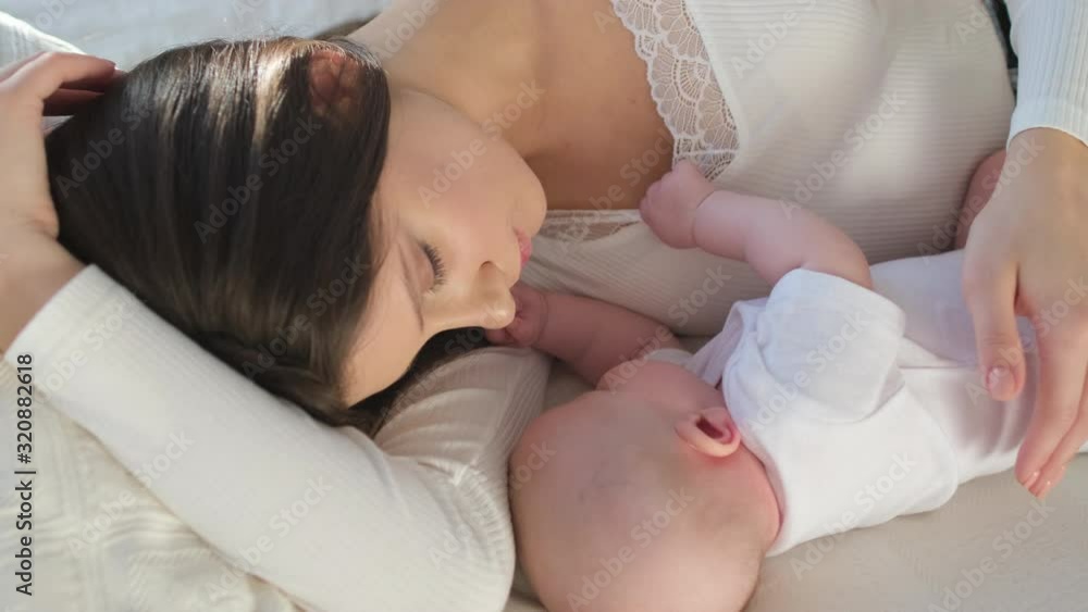 Happy family. Portrait of mother and newborn baby girl kissing hugging in bed. Maternity Parenthood Motherhood. Loving mom enjoying caring playing with little child. healthy childcare. 4 K Slow-motion Happy family. Portrait of mother and newborn baby girl kissing hugging in bed. Maternity Parenthood Motherhood. Loving mom enjoying caring playing with little child. healthy childcare. 4 K Slow-motion