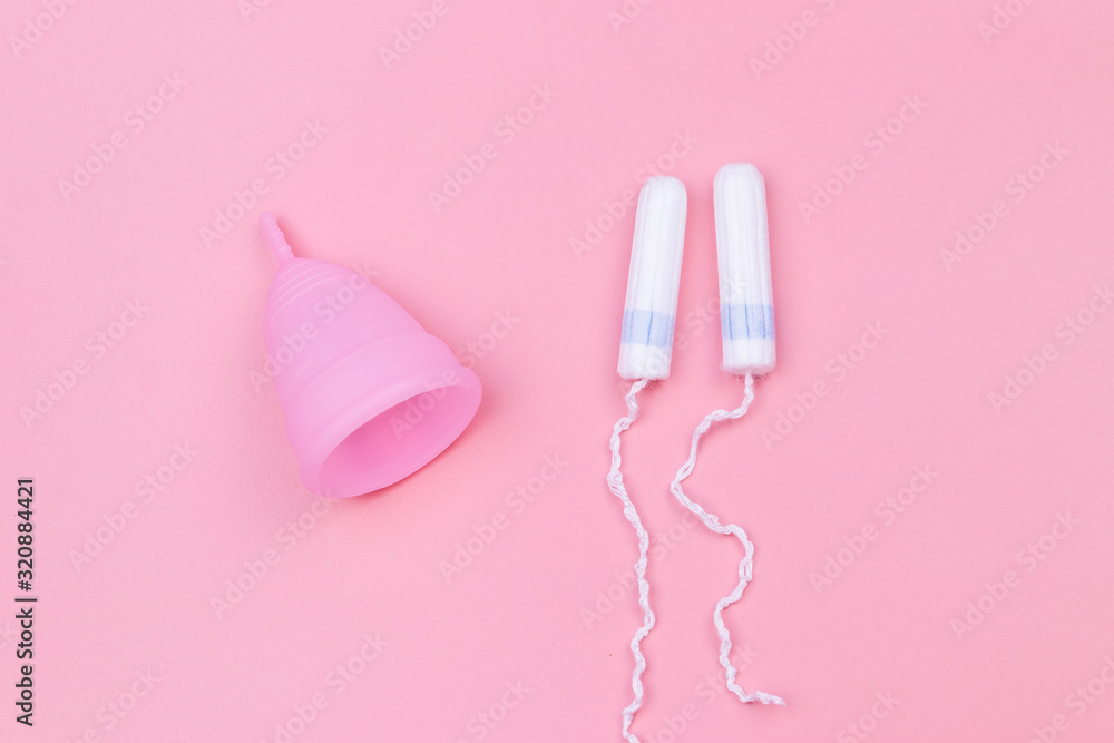 Pink reusable silicone menstrual cup and tampons on pink background. Top view. Concept of feminine hygiene, gynecology and health