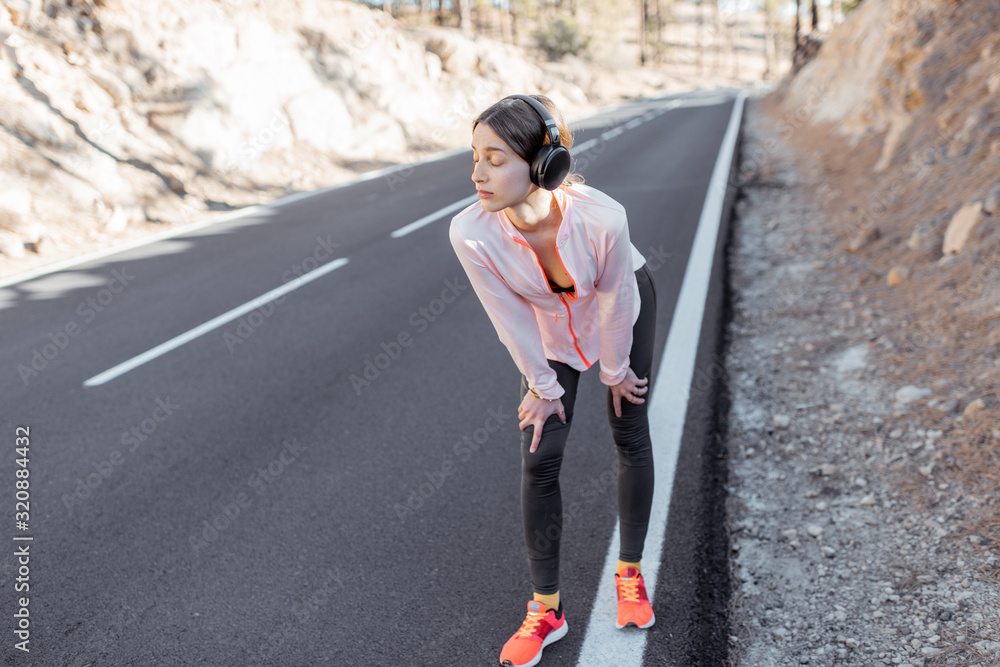 Young woman in sportswear stretching on the beautiful road, training outdoors in the mountains