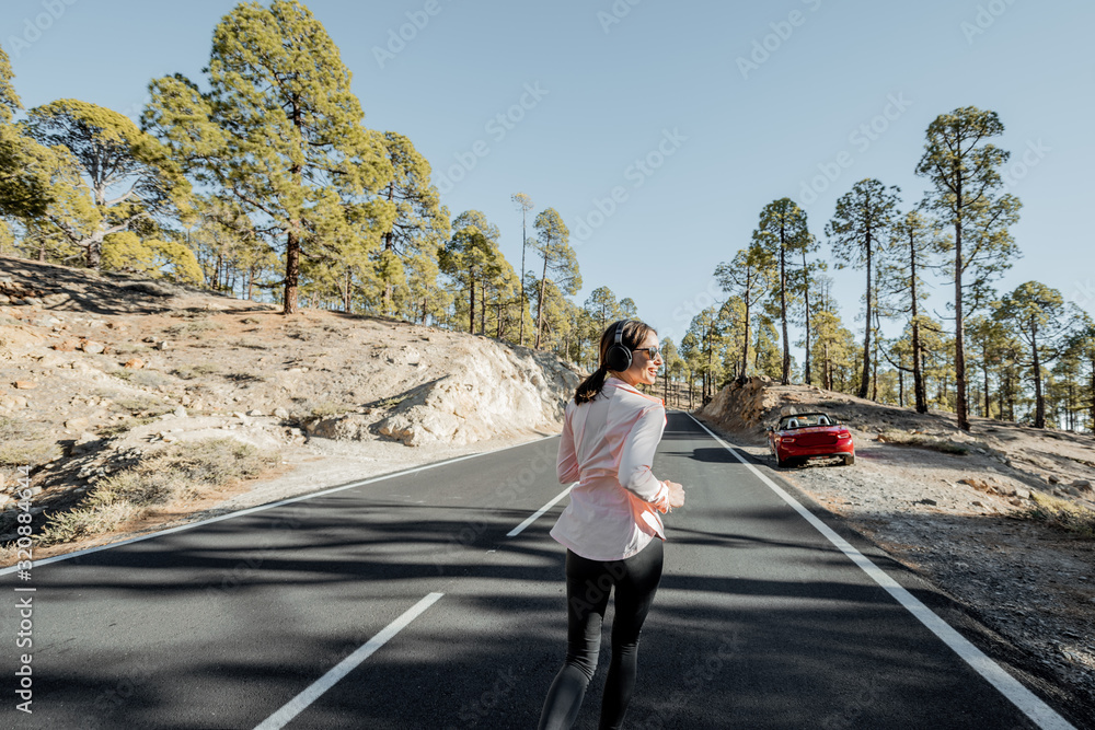 Young woman in sportswear jogging on the beautiful mountain road in the forest, wide view from the backside Young woman in sportswear jogging on the beautiful mountain road in the forest, wide view from the backside