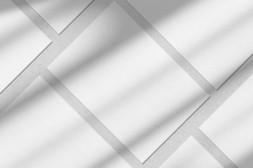 Empty white vertical rectangle poster or business card mockups with diagonal window shadow on the gray concrete wall.Flat lay, top view. For advertising, brand design, stationery presentation.