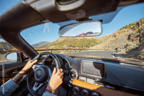 Woman driving car on the mountain road, close-up view with back focus on the road. Road trip concept