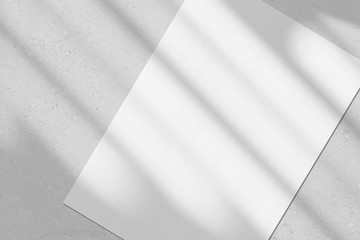 Empty white vertical rectangle poster or business card mockup with diagonal window shadow on the smooth gray concrete wall.Flat lay, top view. Open composition.
