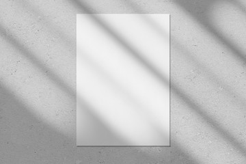 Empty white vertical rectangle poster or business card mockup with diagonal window shadow on the smooth gray concrete wall.Flat lay, top view. For advertising, brand design, stationery presentation.