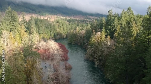 Drone flying backward ten meters above the Cowichan river in winter with trees and clouds . photo