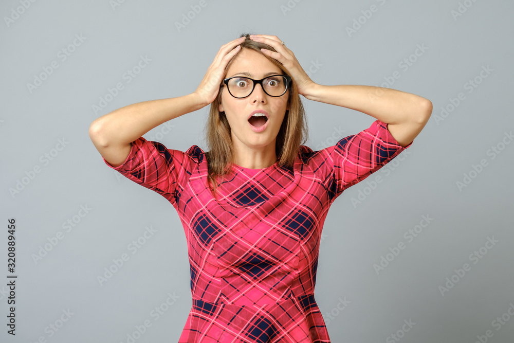 Portrait of stunned woman in red dress, holding hands on head Portrait of stunned woman in red dress, holding hands on head