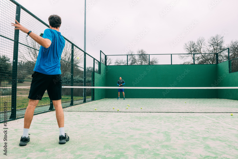 Obraz premium Young man playing paddle tennis on a green court, wearing a blue t-shirt.Sports concept.Copy space