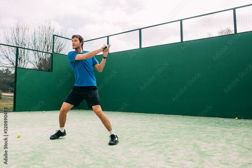 Young man playing paddle tennis on a green court, wearing a blue t-shirt.Sports concept.Copy space