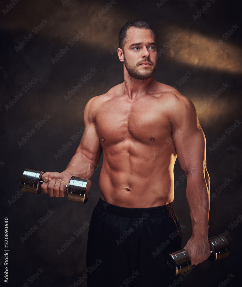 Attractive muscular man is doing exercises with dumbbells at dark room. Attractive muscular man is doing exercises with dumbbells at dark room.