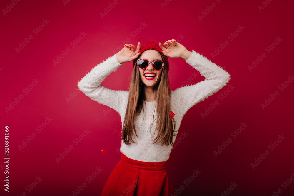 Cheerful girl in fluffy sweater dancing in claret background. Slim long-haired brunette female model in glasses fooling around in studio. Cheerful girl in fluffy sweater dancing in claret background. Slim long-haired brunette female model in glasses fooling around in studio.