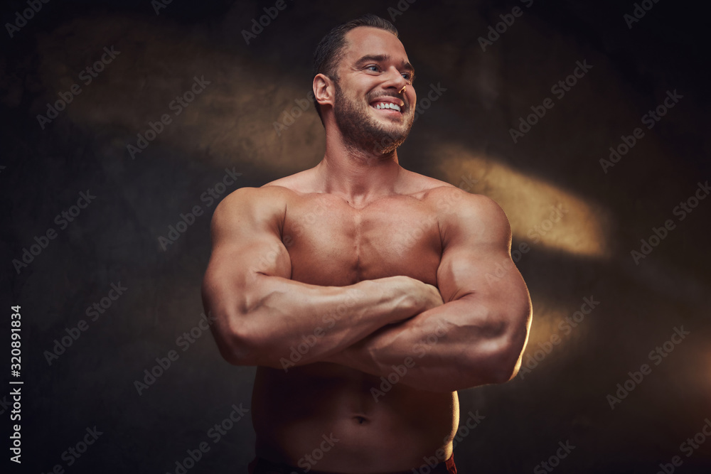 Fototapeta premium Portrait of attractive muscular bodybuilder at dark photo studio with blinks of light.