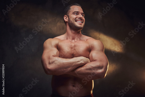 Portrait of attractive muscular bodybuilder at dark photo studio with blinks of light. © Fxquadro