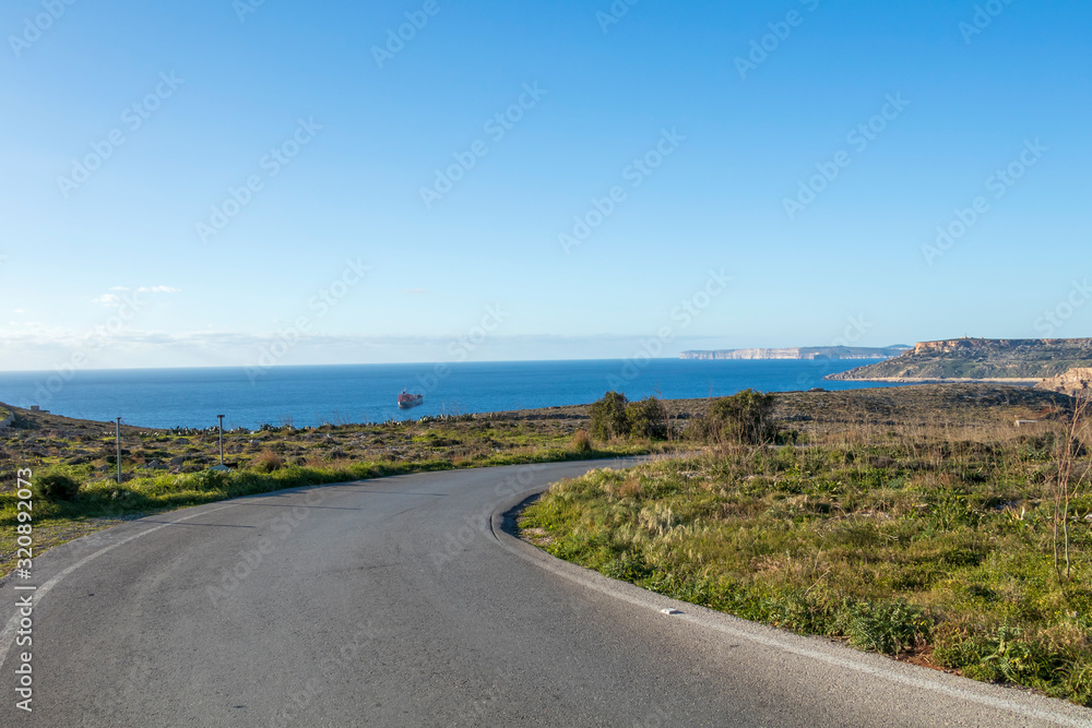 Empty countryside road in Malta surrounded by fields under blue sky in sunny winter day with nobody