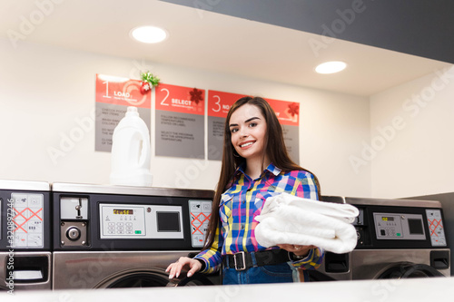 Slika na platnu Girl with clean white towels stands on the background of washing machines in public laundry
