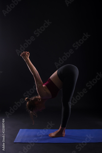 Young attractive woman practicing yoga, on black background, and doing some stretching exercises.